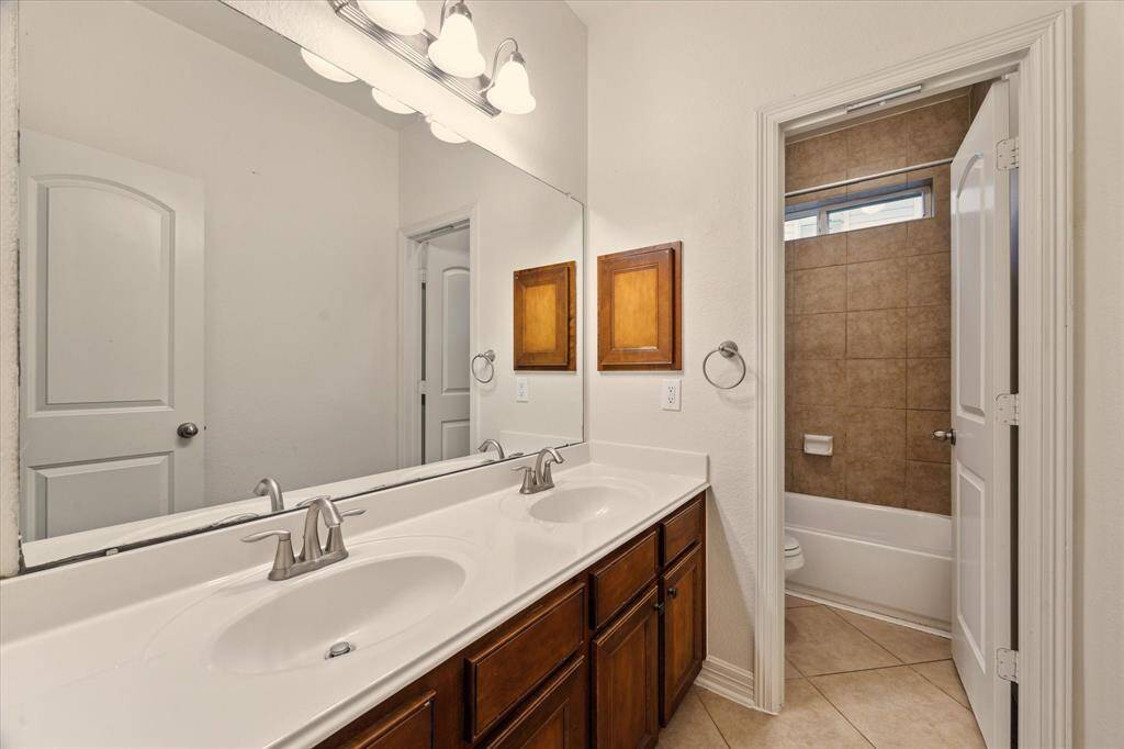 This well-appointed bathroom features a double-sink vanity, ample cabinet storage, and a separate shower/tub combo with tiled surround.