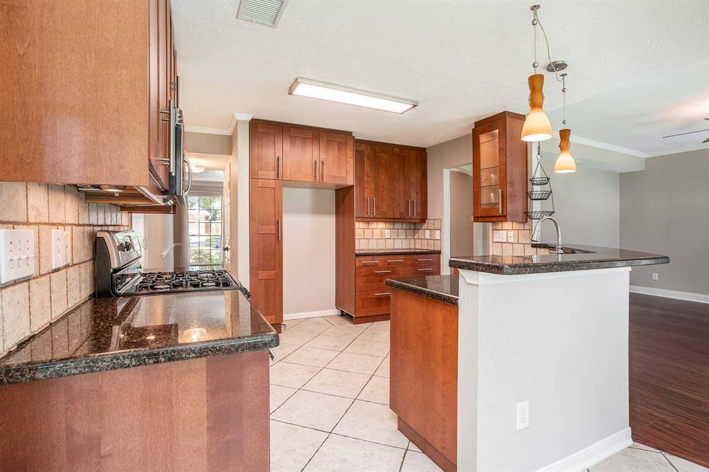 The kitchen features rich wood cabinetry, granite countertops, and a tile backsplash. With a gas range, stainless appliances, and bar seating, it's both functional and stylish—perfect for cooking and entertaining.