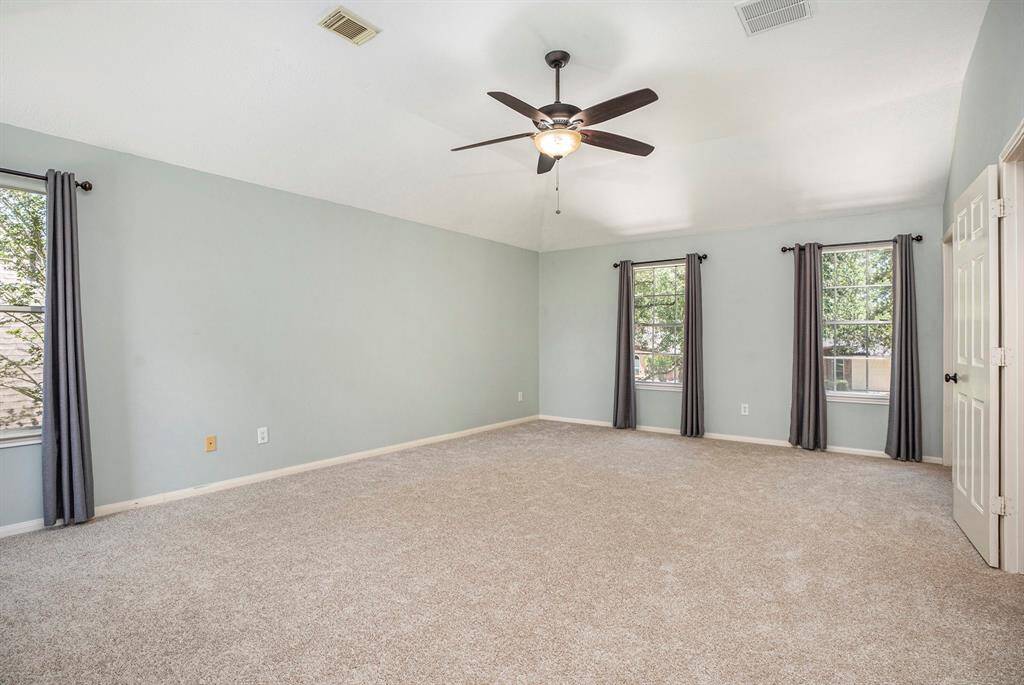 The spacious primary bedroom features soft carpet, multiple windows for natural light, and a ceiling fan for comfort. It also includes two walk-in closets, offering plenty of storage space.