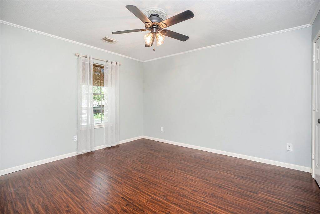 This secondary bedroom features crown molding, a ceiling fan, and a large window that brings in plenty of natural light. The space feels bright, open, and comfortable.