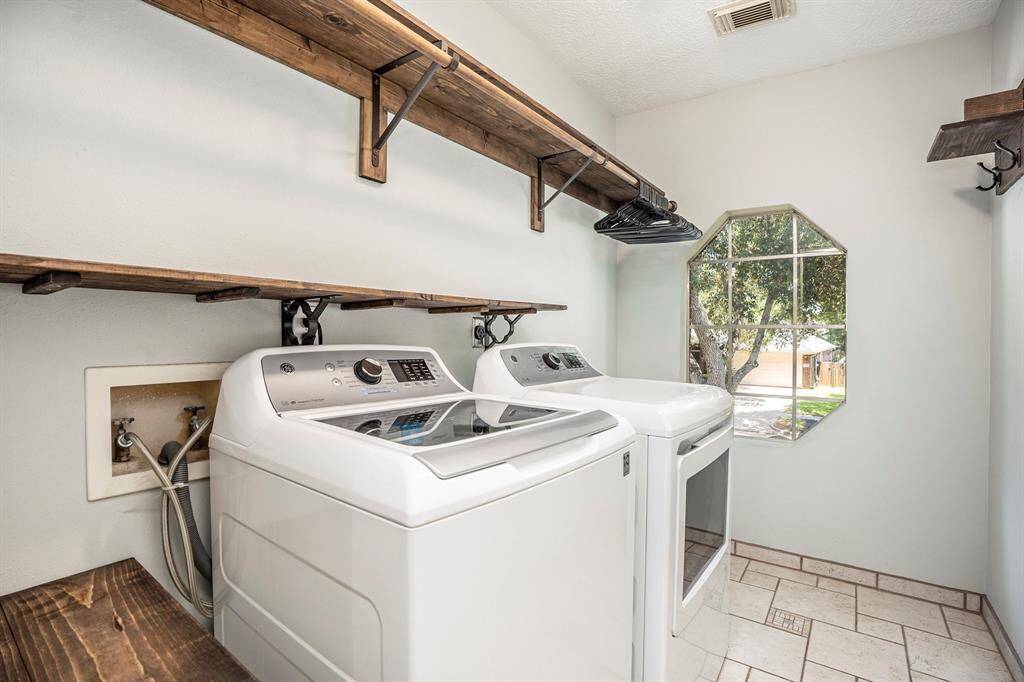 The laundry room offers plenty of natural light, built-in shelving, and a hanging rod for convenience. There's ample space to keep things organized and functional.