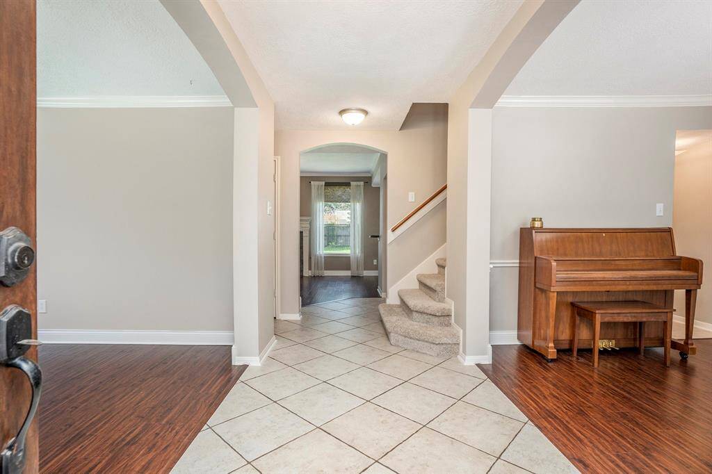Bright and welcoming entry with tile floors, arched openings, and natural light. Wood-look floors add warmth, and the staircase leads to the second floor.