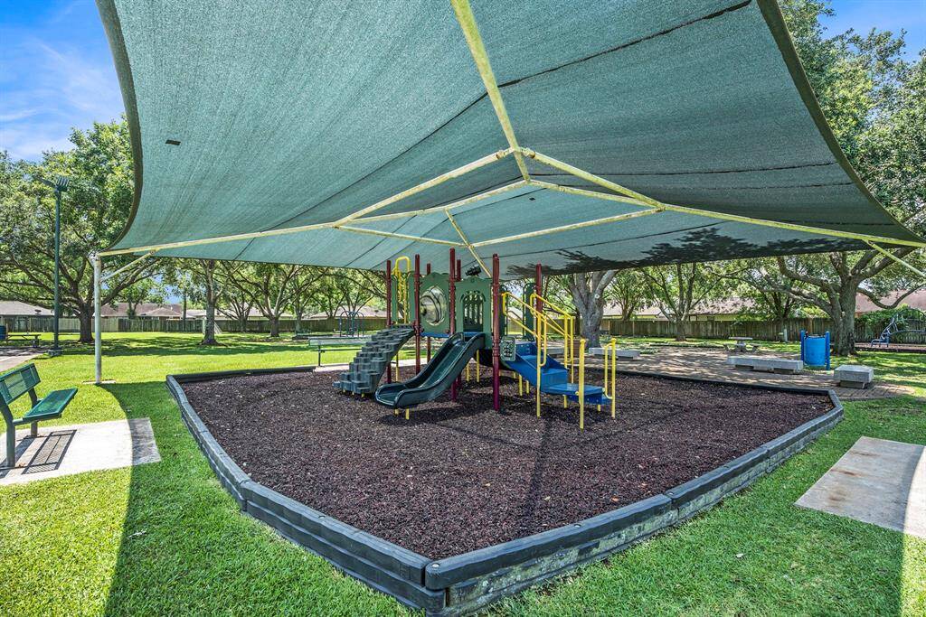 This section of the community park includes a shaded playground area, ideal for outdoor enjoyment and staying cool. Surrounded by open green space and seating, it’s a great spot to relax or unwind.