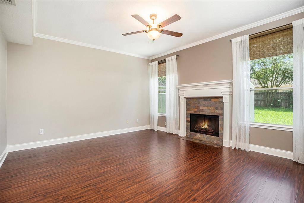 The living room features rich wood-look flooring, large windows with backyard views, and a cozy fireplace with a stone surround—creating a warm and inviting space to relax.