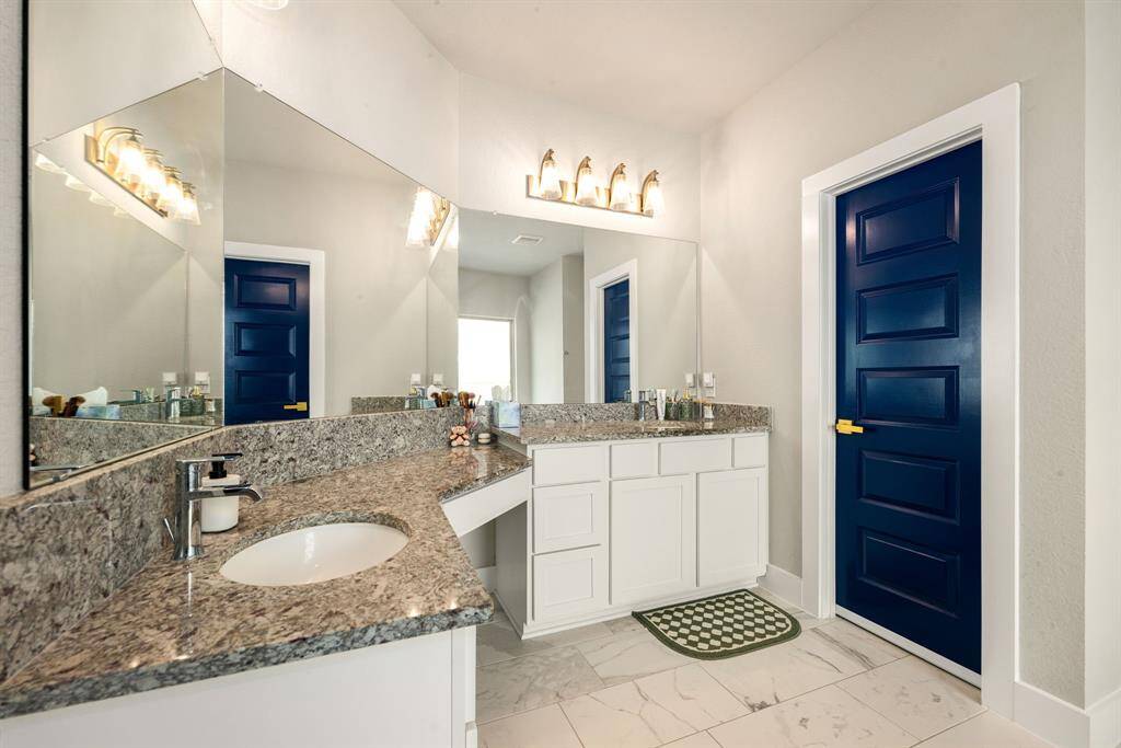 Bright and modern ensuite bath featuring sleek granite countertops, fresh white cabinetry, and a striking navy door, complete with a spacious vanity area and elegant fixtures that create a spa-like atmosphere.