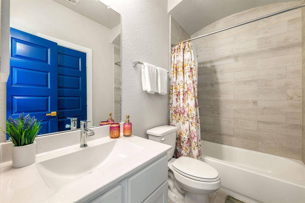 Secondary bathroom features light countertops and cabinets, custom paint, shower/tub combo with tile surround, large mirror, tile floors, sleek fixtures and modern finishes, plenty of space to accommodate any visiting family or guests.