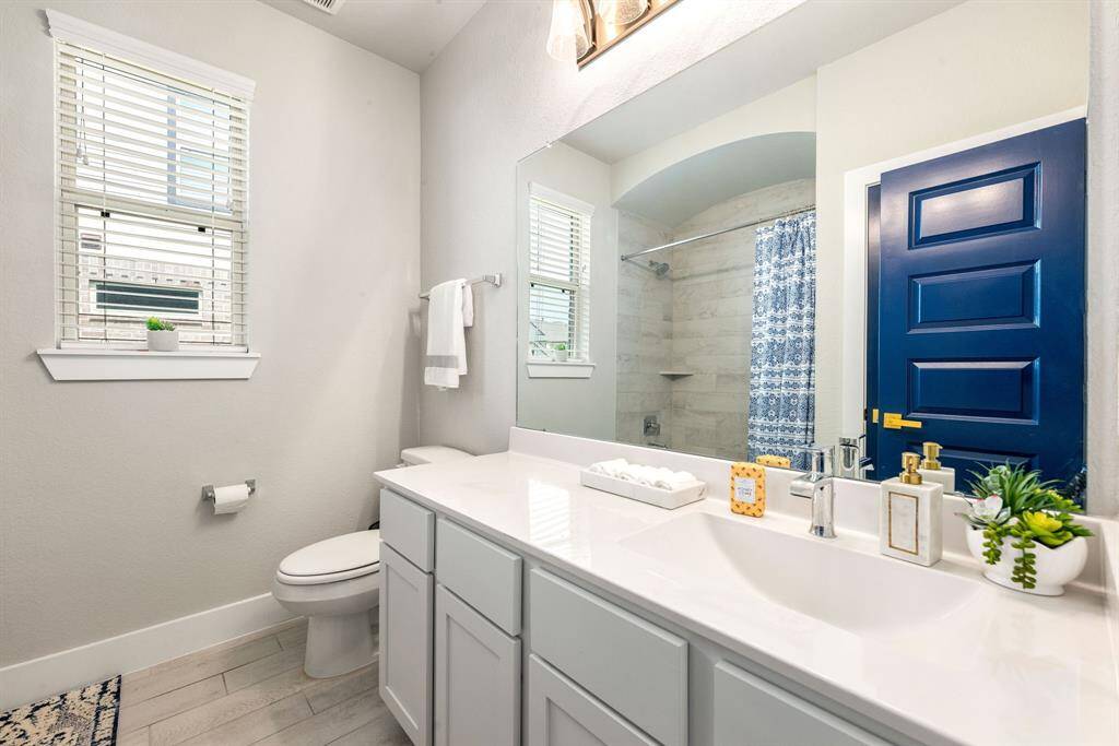 Secondary bath features tile flooring, bath/shower combo with tile surround, dark wood cabinets, beautiful light countertops, mirror, dark, sleek fixtures and modern finishes.