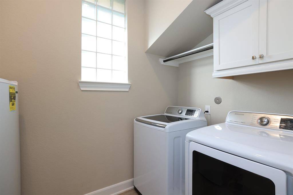 The utility room is thoughtfully designed with a built-in hanging rod and upper cabinets for extra storage, all in a convenient location within the home, making laundry tasks both efficient and organized.