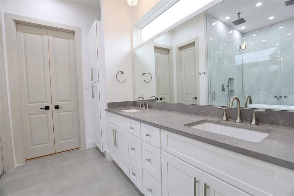 This stylish primary en suite features ample storage with dual drawer sets, a leather-finished 3 CM quartz countertop, and a striking designer faucet. A custom wall-to-wall mirror is topped by a sleek horizontal privacy window, brightening the space with soft, natural light.