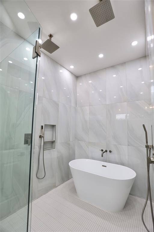 Indulge in a spa-like experience  with dual rainfall shower heads and separate handhelds for a personalized experience. Floor-to-ceiling tile in soft gray with warm, flowing swirls sets a tranquil tone.