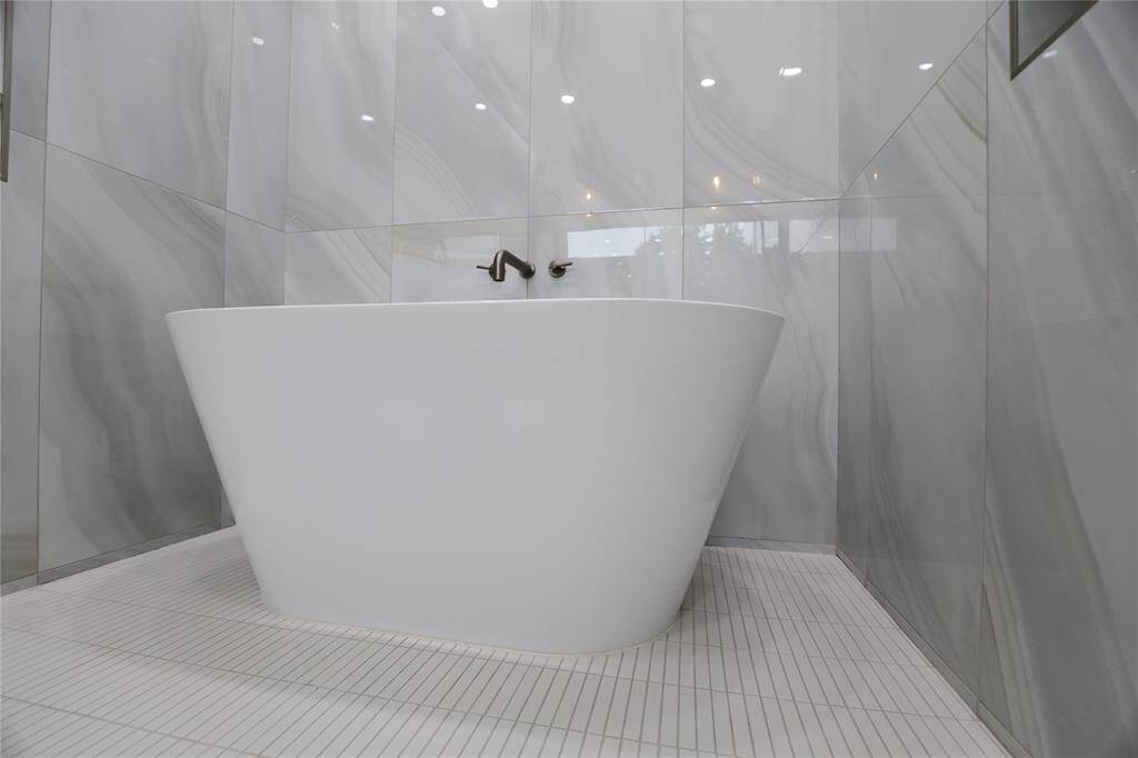 A stunning Woodbridge soaking tub is beautifully surrounded by large-profile tiles, creating a serene, spa-like ambiance that complements the rest of the en suite.