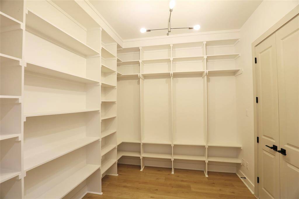 The primary suite closet boasts floor-to-ceiling custom carpentry, with a shelved area designed to showcase your shoe collection, including space for cowboy boots. The upper shelves offer the perfect spot for displaying hats or bags, blending both functionality and style. A beautiful chandelier adds an elegant warmth to the room.