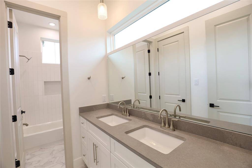 This Jack and Jill bathroom features a custom-sized mirror perfectly completing the space, two sets of drawers, and a specialty imported leather quartz counters. A horizontal window above fills the space with natural light while maintaining privacy.