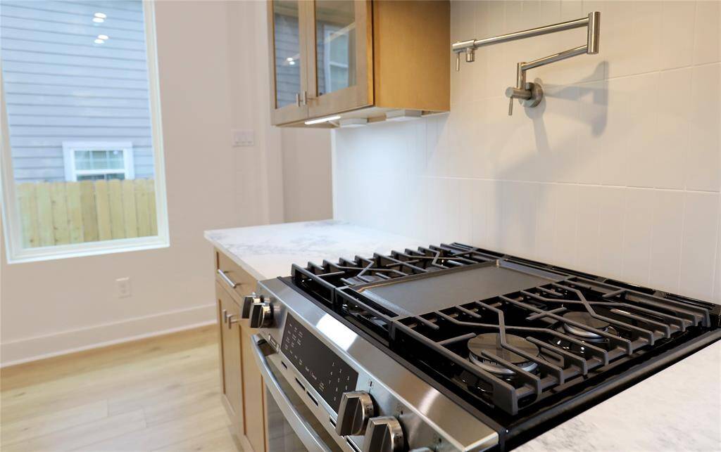 The gas range with a built-in griddle and overhead pot filler anchors this stylish, chef-ready kitchen. Notice the uninterrupted backsplash, the outlets are hidden beneath the cabinetry.