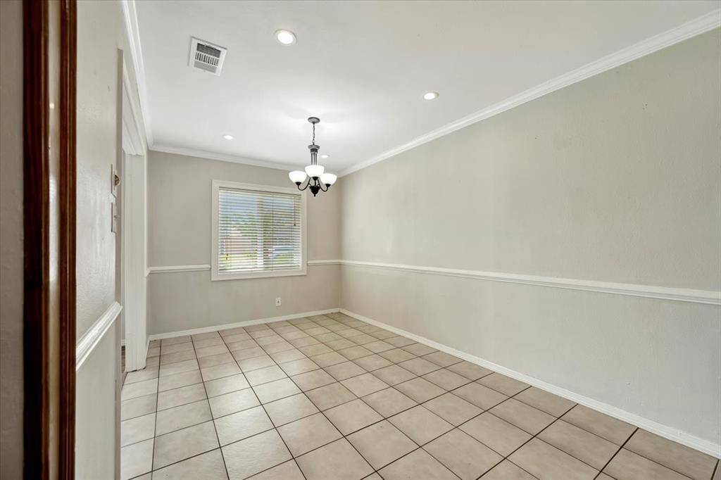 Bright dining room with neutral tones, tile flooring, and a central chandelier. Features a large window for natural light and crown molding for an elegant touch.