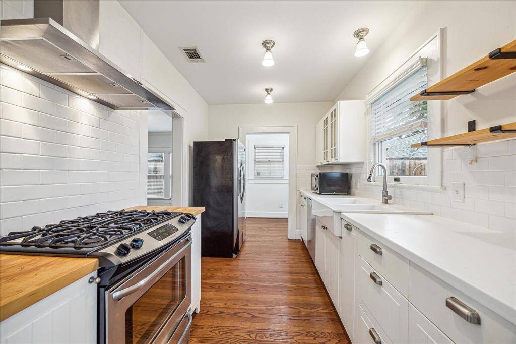 The stunning galley Kitchen boasts sleek countertops, timeless backsplash, ample storage, and modern floating shelves, all beautifully complemented by rich hardwood floors.  West end of Kitchen opens to designated sun room or office space.