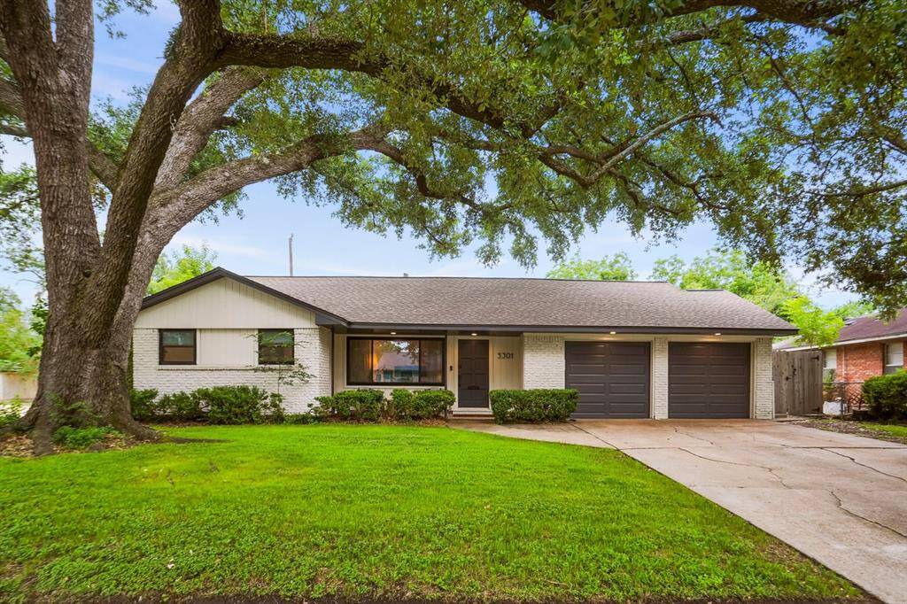 Charming single-story home with a painted brick exterior, (SW Masion Blanche) and dark garage doors, (SW Iron Ore). Features a spacious front yard with a large, mature tree providing ample shade. The house has a welcoming front entrance and dual garage, perfect for a family setting.