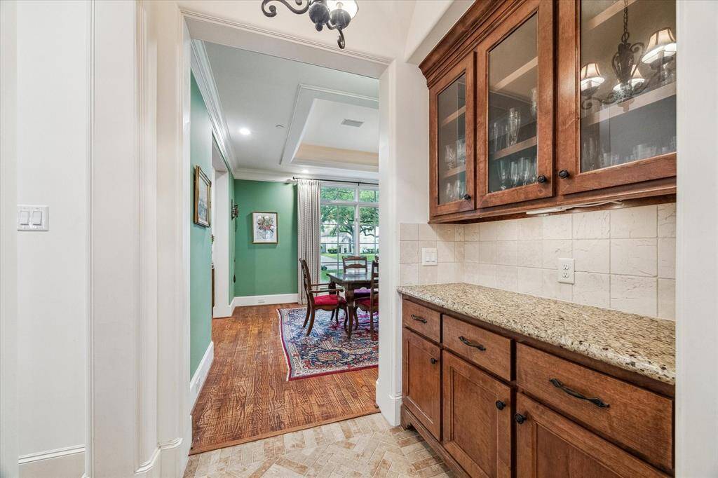 This butler’s pantry features granite countertops, a tile backsplash, and ample upper and lower cabinetry for additional storage. The space offers a convenient transition between the kitchen and formal dining room, ideal for staging and serving.