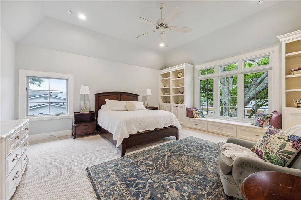 This secondary bedroom features vaulted ceilings, large windows with a built-in bench, and integrated shelving for added storage. The room is carpeted, well-lit with recessed lighting and natural light, and offers views of the surrounding trees and neighborhood. Could also be used as a 2nd Primary Bedroom.