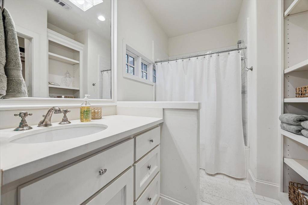 This secondary bath includes a single-sink vanity with ample drawer storage, a built-in shelving unit, and a combination tub and shower with a tile surround. A small horizontal window provides natural light, and the layout is compact yet functional.