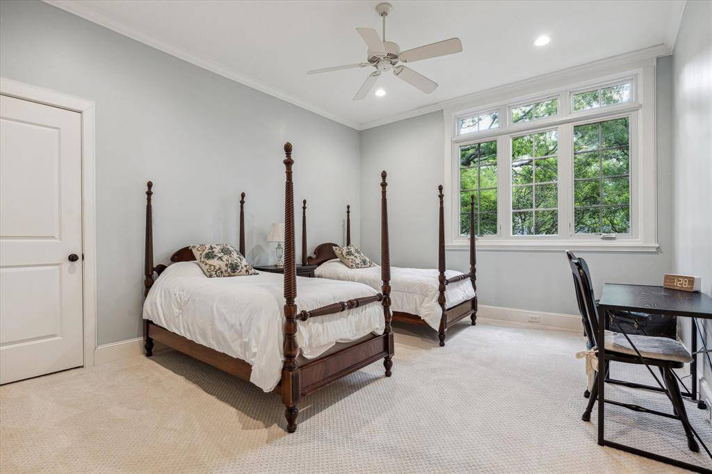 This secondary bedroom offers a spacious layout with high ceilings, crown molding, and large windows that provide ample natural light and views of the surrounding trees. It is carpeted and includes recessed lighting and a ceiling fan for added comfort.