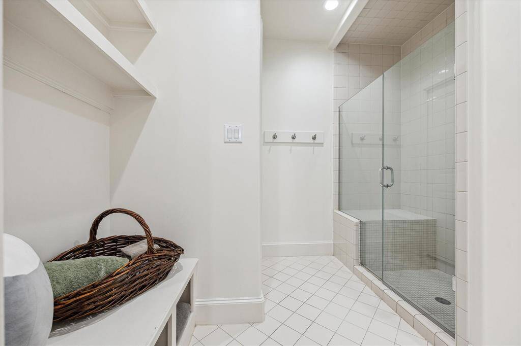 This secondary Hollywood bath features a walk-in shower with a built-in bench and glass enclosure, tiled walls and flooring, and built-in shelving for storage. The layout is functional and designed for shared use, with a clean and streamlined configuration.