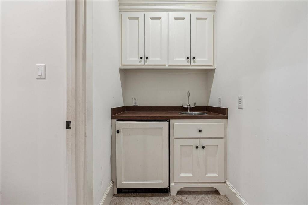 This game room bar area features upper and lower cabinetry, a small sink, and a built-in under-counter refrigerator. The compact layout provides convenient functionality for serving and storage within the game room space.