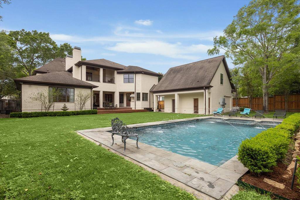 This backyard features an expansive lawn with plenty of open green space and a large rectangular pool equipped with multiple water features. The pool is surrounded by a stone deck and bordered by neatly trimmed landscaping. The yard offers a spacious layout ideal for recreation and outdoor activities.