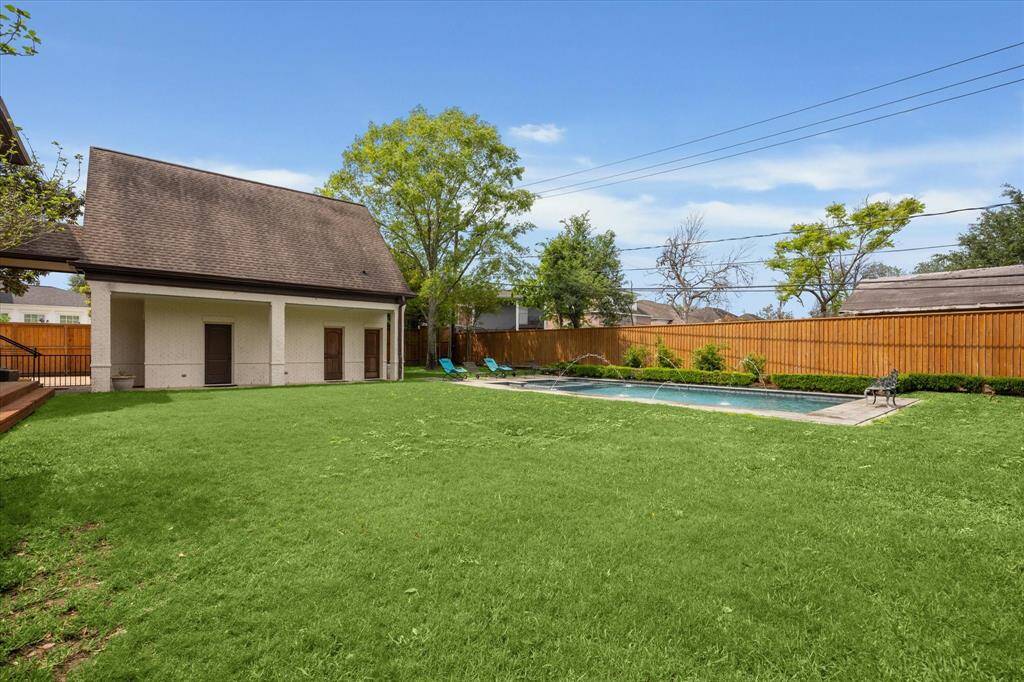This backyard offers a large, open grassy area ideal for recreation and outdoor activities. A spacious pool with water features is set along one side, bordered by landscaping and a stone deck. The expansive lawn provides ample space for play or entertaining.