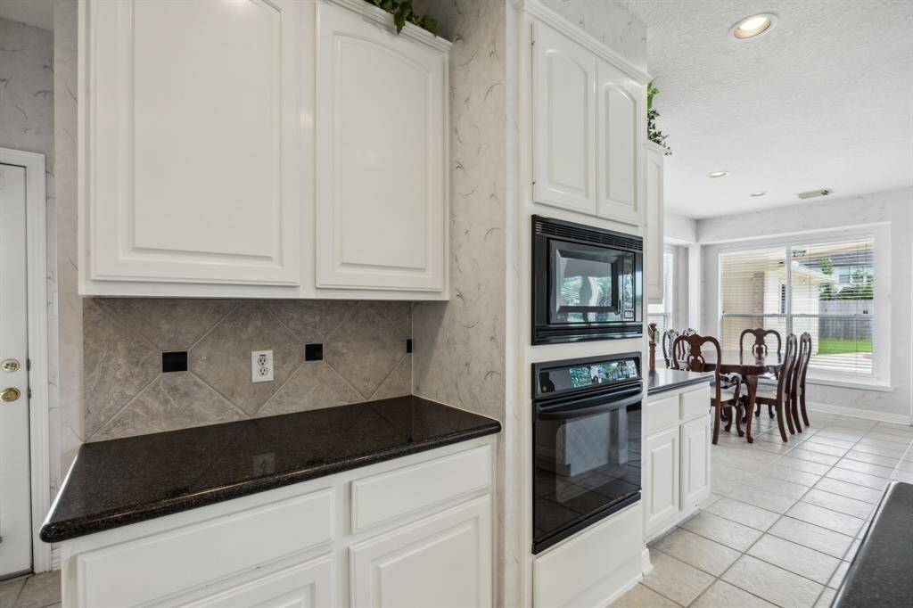 This wall of built-ins not only maximizes counter space but also contributes to the streamlined, functional layout. The adjacent electric cooktop is ideally located for preparing meals while engaging with family or guests in the living area. Ample cabinetry provides generous storage, while large windows invite natural light to fill the space, creating a bright and welcoming ambiance