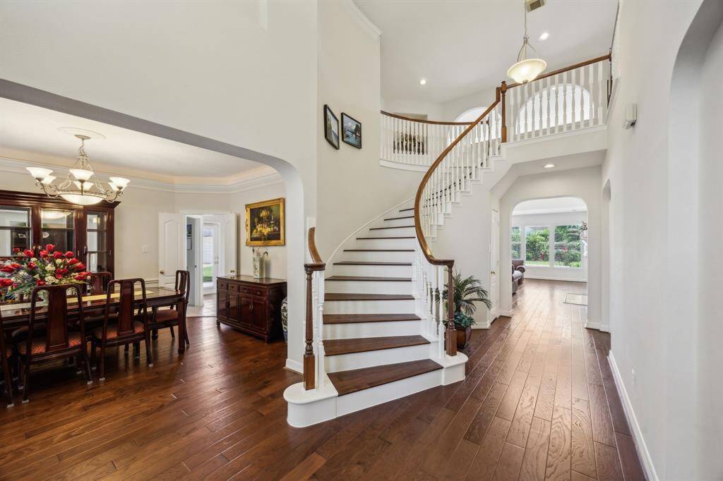 A curved staircase adds architectural elegance the moment you step inside, setting the tone for the refined design that flows throughout the home. The grand entryway is filled with natural light and soaring ceilings, creating a welcoming ambiance that’s both impressive and inviting. Rich hardwood floors and detailed trim work highlight the craftsmanship, while open sightlines offer a seamless connection to the formal and informal living spaces beyond.