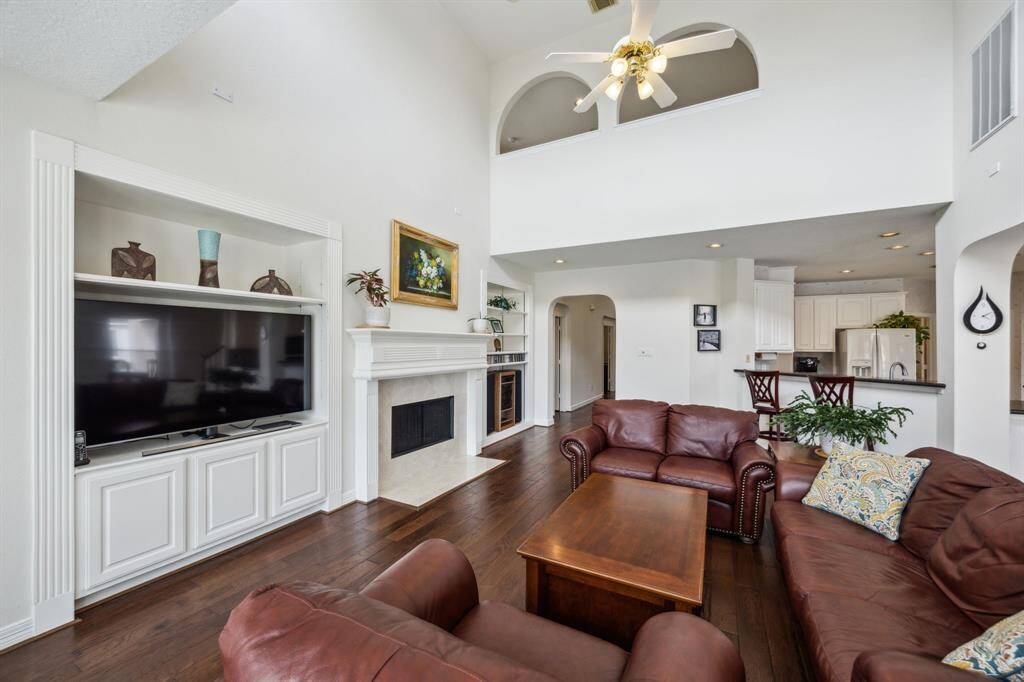 Flowing seamlessly from the grand entry, the living area is the heart of the home. Design to impress and inspire. Soaring ceilings create a sense of openness and grandeur, while expansive windows flood the space with natural light, enhancing the warmth of the rich wood flooring. A beautifully centered fireplace serves as a stunning focal point, flanked by two custom built-in shelves that offer both style and storage.