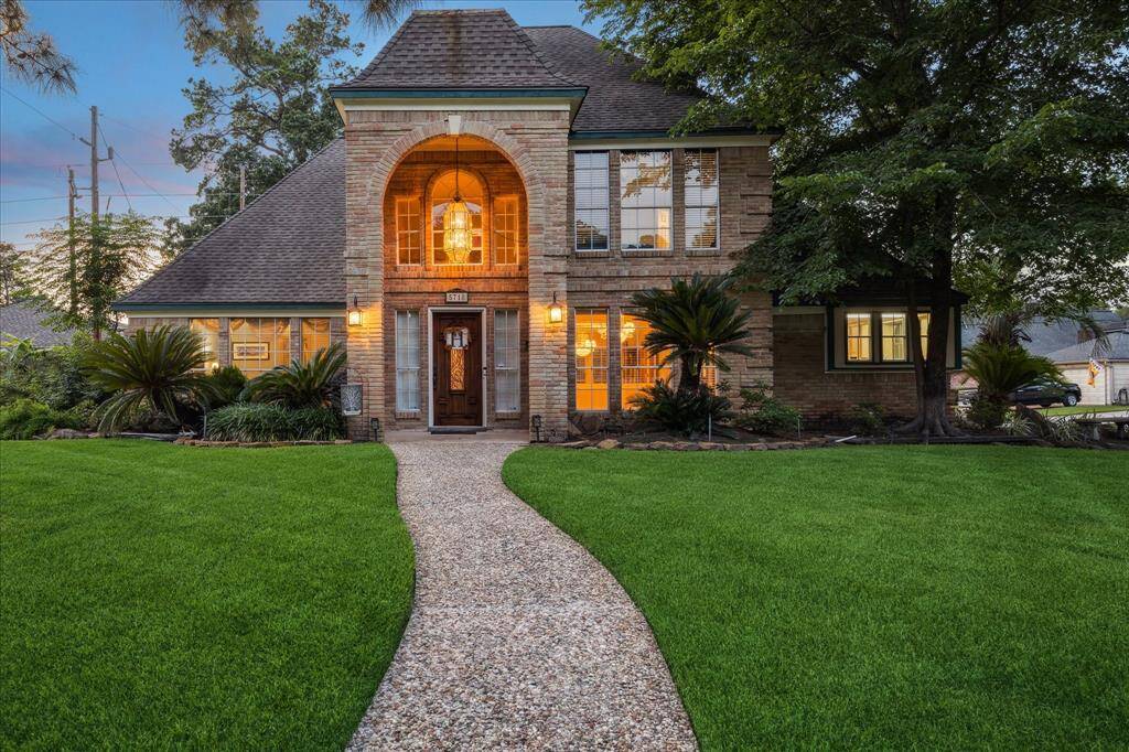 This charming two-story home features a warm brick exterior, large windows, and a welcoming front walkway. The well-maintained lawn and mature trees create an inviting curb appeal.