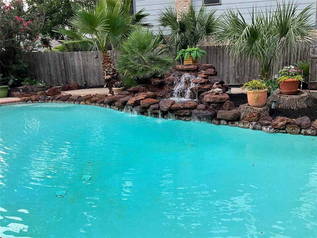 This backyard  features a sparkling chlorine or saltwater pool with a charming rock waterfall, surrounded by lush palm trees and greenery, creating a perfect oasis for relaxation and entertainment.