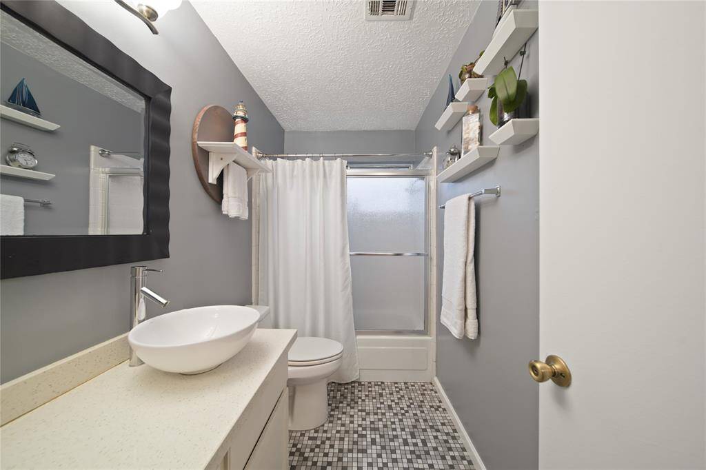 Step into a beautifully designed bathroom that exudes contemporary charm. Featuring a sleek vessel sink and granite countertop, this space is complemented by a stylish framed mirror. Enjoy the convenience of a shower-tub combo with a chic frosted glass door, set against stylish gray walls.