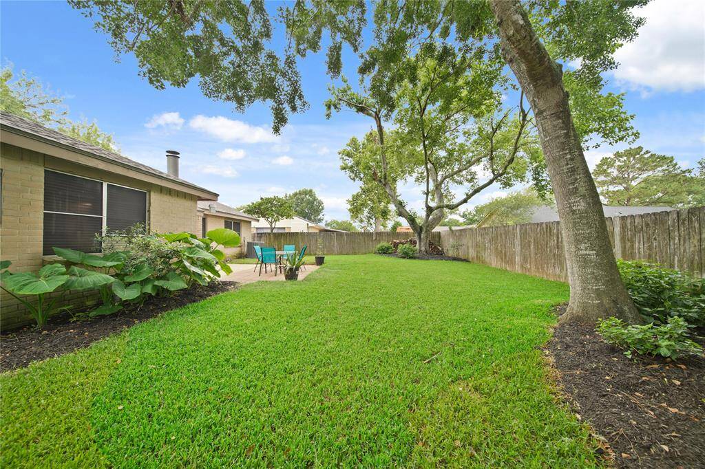 This backyard features a spacious, well-maintained lawn with lush greenery and mature trees providing shade.