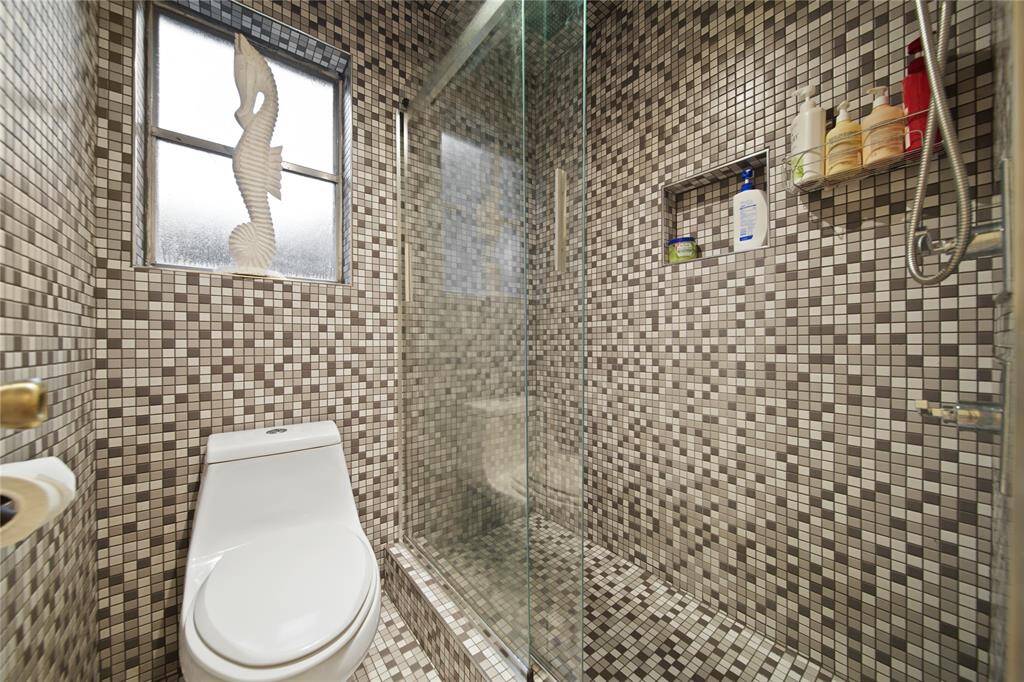 Step into a spa-like retreat in the primary bathroom where modern design meets elegant functionality. The space boasts stunning mosaic tile walls and ceiling that create a unique and sophistsicated ambiance. Enjoy the sleek glass-enclosed shower that complements the room's contemporary aesthetics, while a frosted window ensures natural light pours in, maintaining privacy and enhancing the tranquil atmosphere.