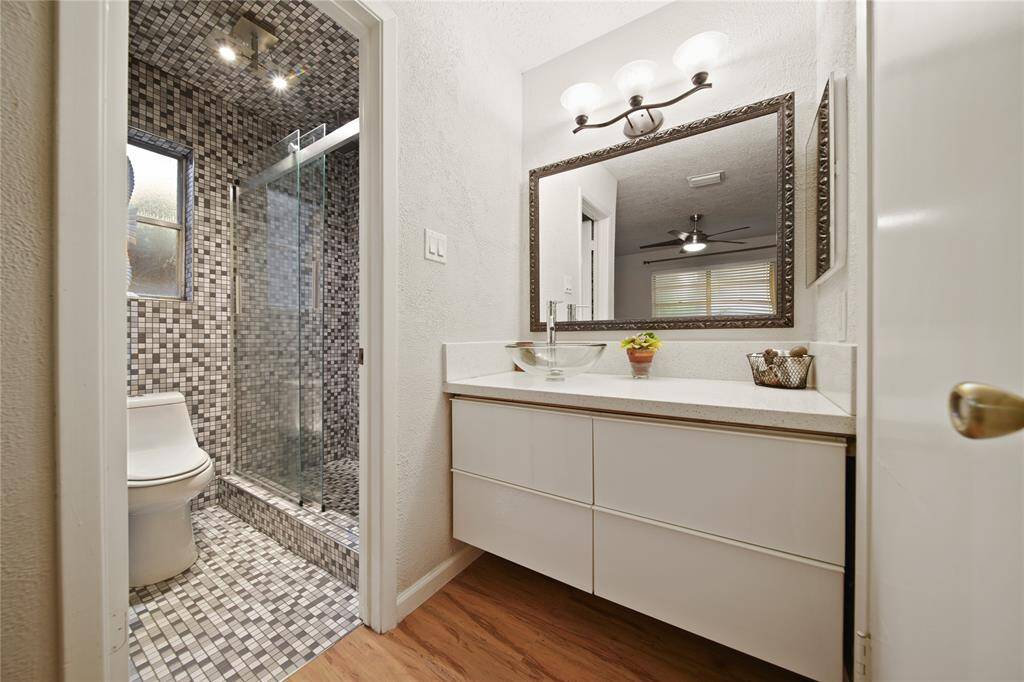 The modern vanity features a stylish vessel sink and a large, beautifully framed mirror.  The space is enhanced by contemporary lighting fixtures and exquisite wood flooring that seamlessly flows into the spacious primary bedroom.