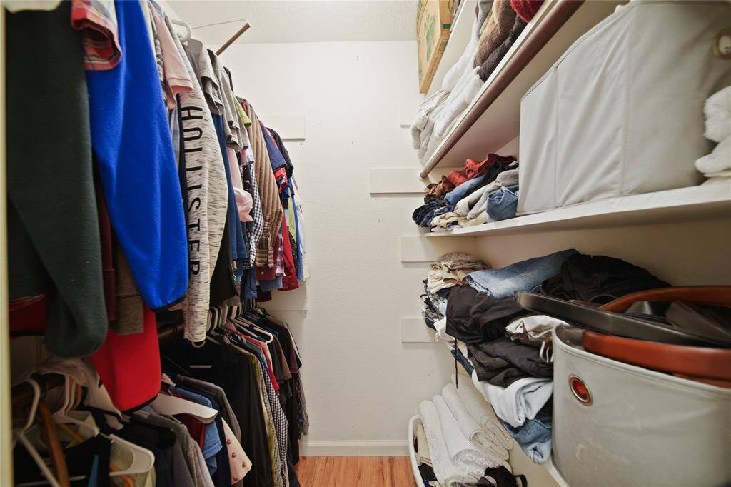This is a well-organized walk-in closet, located off the primary bathroom, featuring hanging space for clothes, neatly arranged shelves for shoes and accessories with a clean, minimalist design.