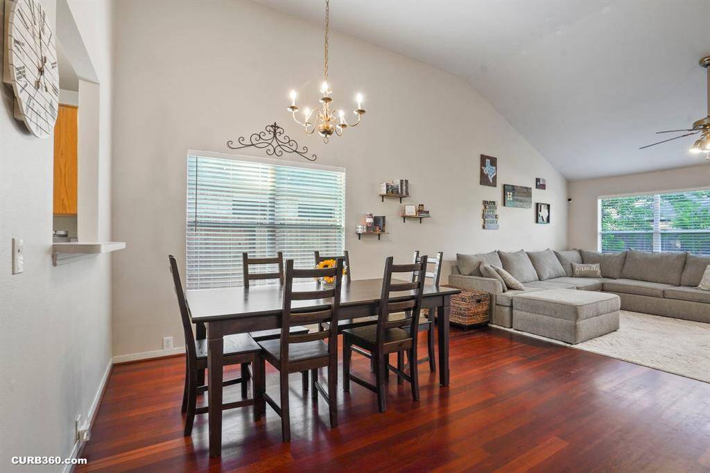 Spacious and inviting living room with high ceilings, rich wooden floors, and abundant natural light. Features a modern ceiling fan, cozy sectional sofa, and stylish decor. French doors lead to a lush backyard, perfect for relaxation and entertaining.