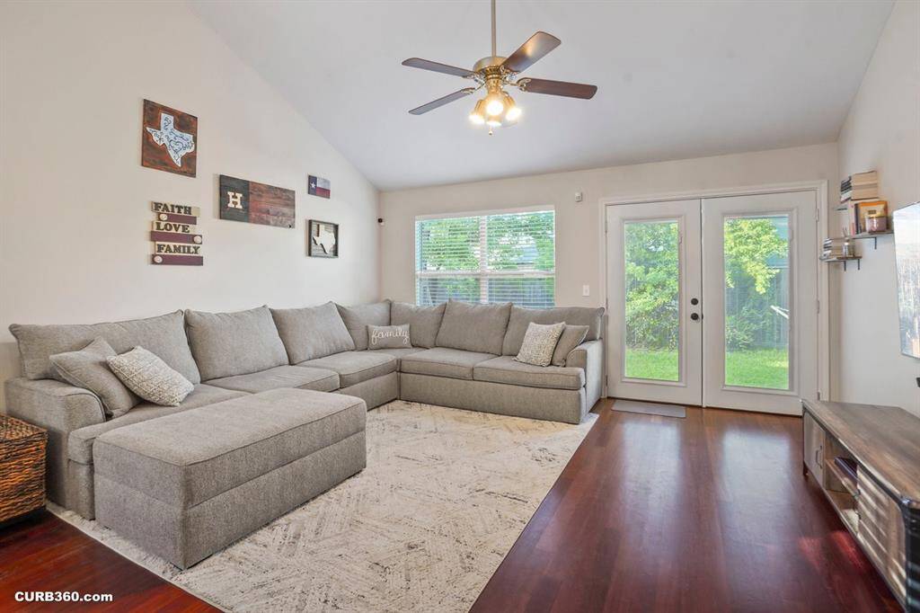Experience comfort and style in this inviting living room, featuring a spacious sectional sofa and rich hardwood floors. Abundant natural light streams through large windows, while French doors seamlessly connect indoor and outdoor living. Perfect for relaxation and entertaining.