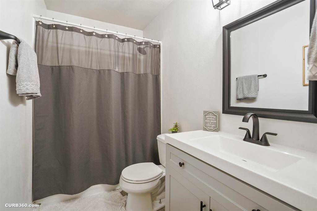 Modern and elegant bathroom featuring a sleek vanity with a stylish black faucet, a spacious mirror, and a soothing gray shower curtain. Ideal for relaxation and convenience.