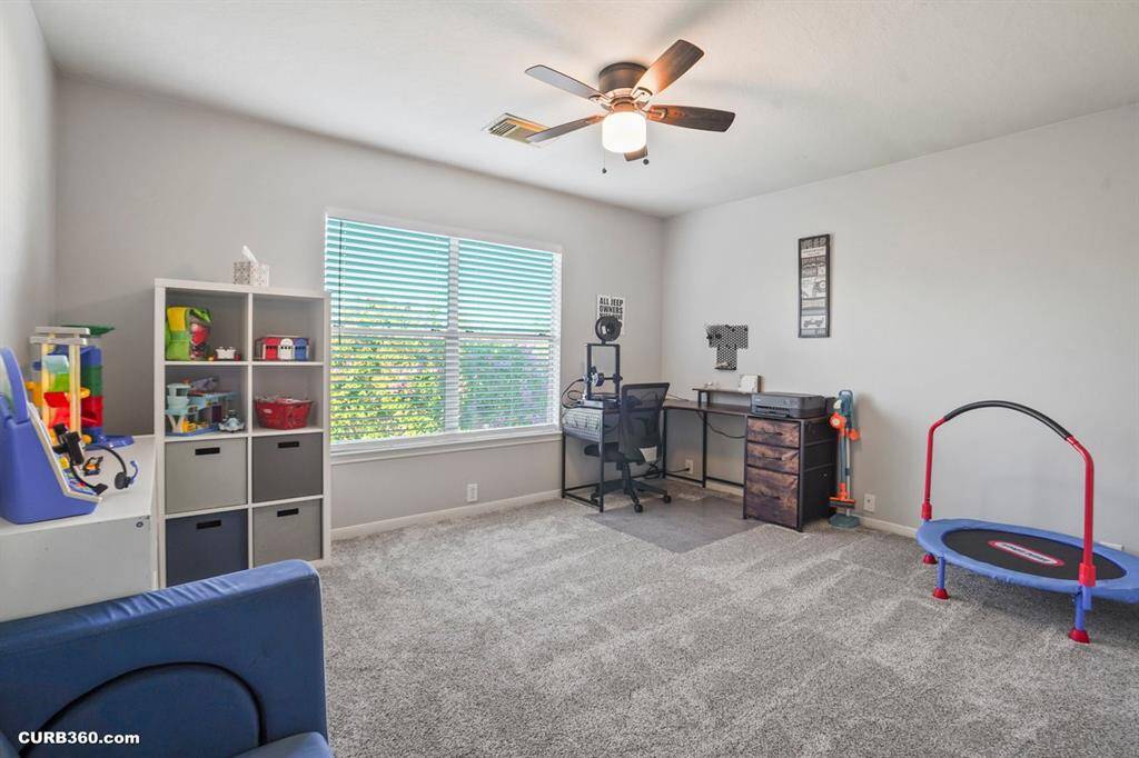 Bright and spacious room perfect for a play area or home office, featuring plush carpet, a large window for natural light, and a ceiling fan for comfort.