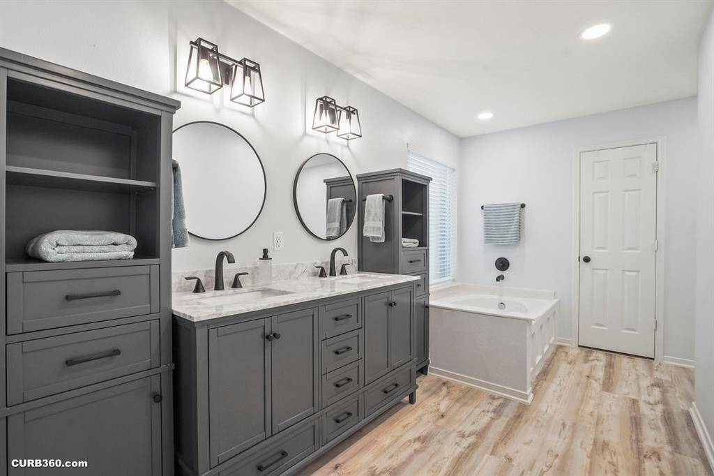Experience luxury in this beautifully designed bathroom featuring a double vanity with elegant marble countertops and stylish fixtures. Enjoy the spacious bathtub and ample storage, all set against sleek wood flooring for a modern touch. Perfect for unwinding and relaxation.