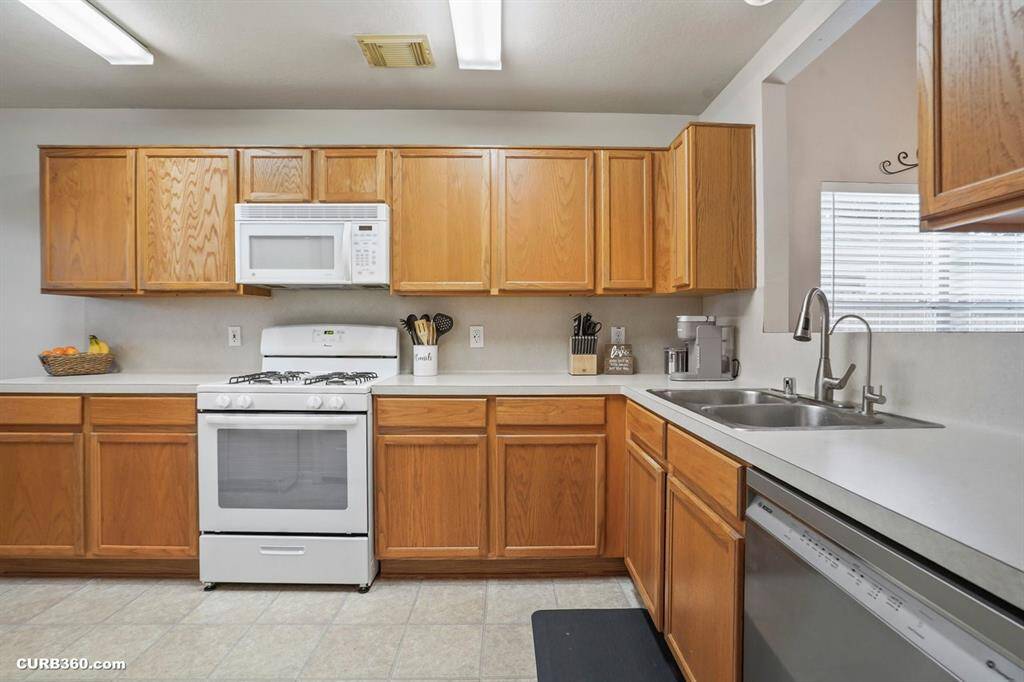 Modern kitchen featuring ample wooden cabinetry, sleek countertops, and a gas stove. Complete with a built-in microwave, dishwasher, and dual sinks, it offers functionality and style for all your culinary needs.