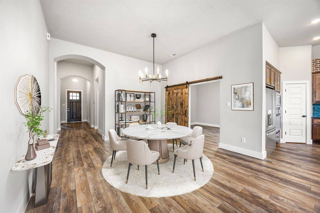 Step into elegance with this stunning entryway, featuring soaring ceilings, rich wood look vinyl plank flooring, and arched hallways that create a grand first impression. A rustic sliding barn door adds character and leads to a versatile space, perfect for a dining room or study. The statement lighting and contrasting accent walls enhance the home’s modern yet warm aesthetic. This inviting layout seamlessly blends style and functionality, making it an ideal retreat.