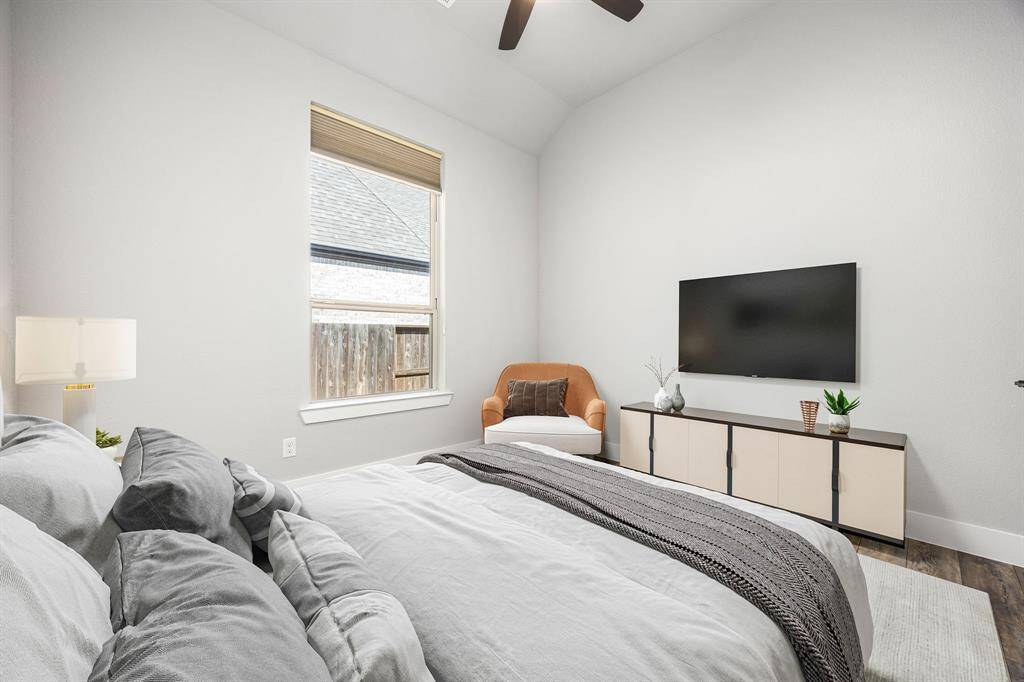 Secondary bedroom features rich vinyl plank floors, neutral paint, dark stained ceiling fan with lighting and a large window with privacy blinds.