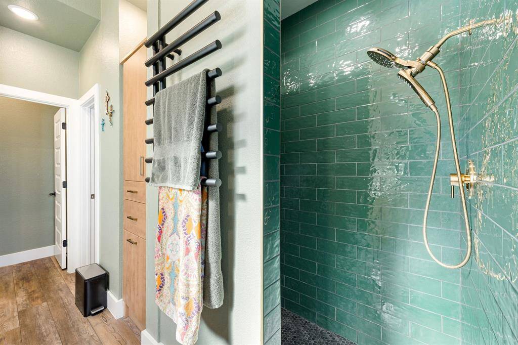 Indulge in spa-like luxury with this stunning walk-in shower, featuring rich emerald green subway tiles, a sleek gold rain showerhead, and modern fixtures. The open-concept design seamlessly flows into a beautifully appointed space with custom cabinetry, elegant wood flooring, and a chic heated towel rack. A perfect blend of style and function, this bathroom is designed for ultimate comfort and sophistication.