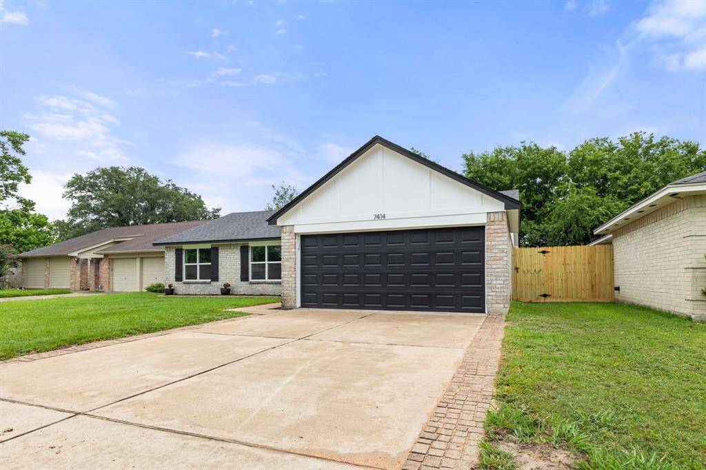 This photo showcases a charming single-story home with a modern black garage door and a spacious driveway. The exterior features light brick and a neatly maintained lawn, offering great curb appeal. A wooden fence provides added privacy.