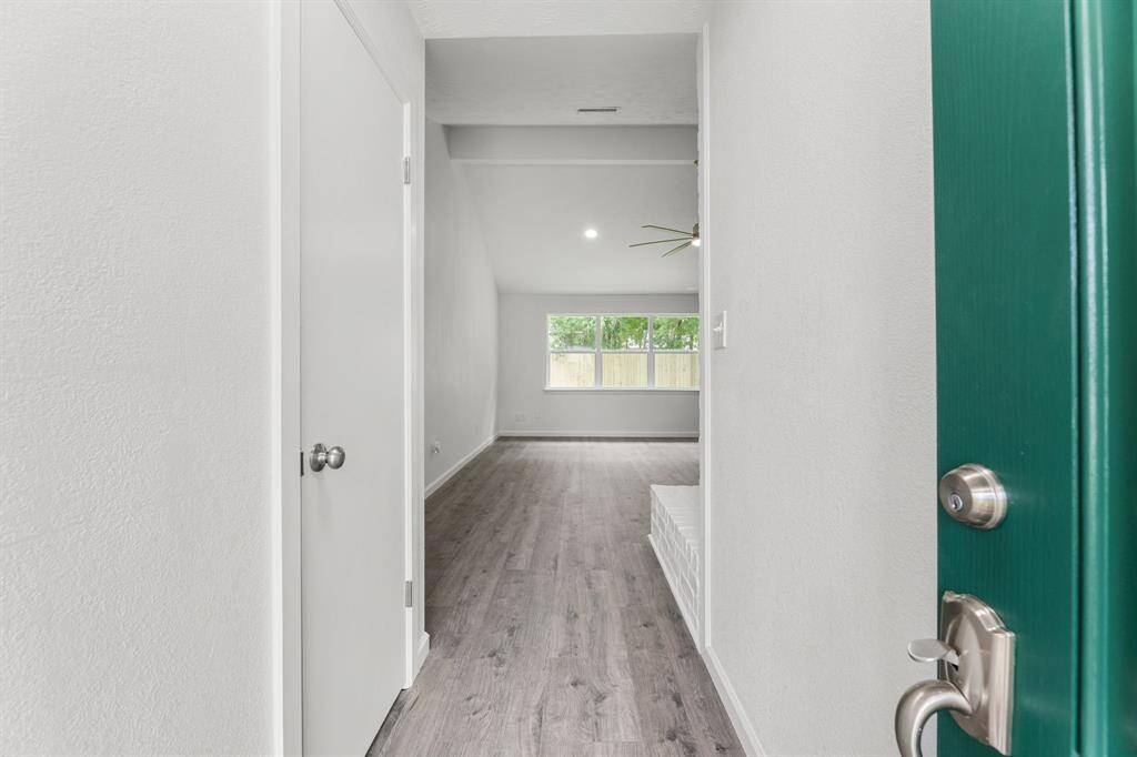 This photo showcases the entryway of a home with a modern, open layout. It features light-colored walls, wood flooring, and a glimpse of a bright living area with large windows. A ceiling fan is visible, adding a modern touch.